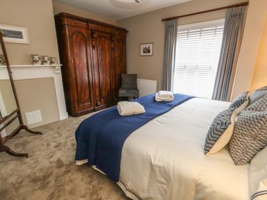 A bedroom with a bed covered with white and blue bedding a wooden wardrobe and a gray chair at Manor Farm House Bere Regis