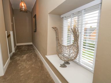 A hallway with carpet flooring a window with blinds and a wicker bird decoration on the windowsill at Manor Farm House Bere Regis