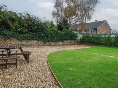 A garden with a wooden picnic table on gravel beside a grass lawn and a brick house in the background at Manor Farm House in Bere Regis
