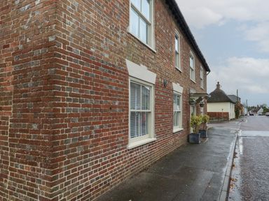 A brick building with white windows and planters on a wet sidewalk at Manor Farm House in Bere Regis