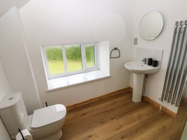 A bathroom with a toilet, sink, round mirror, towel rack, and frosted window at Folly Cottage in Llanteg near Saundersfoot