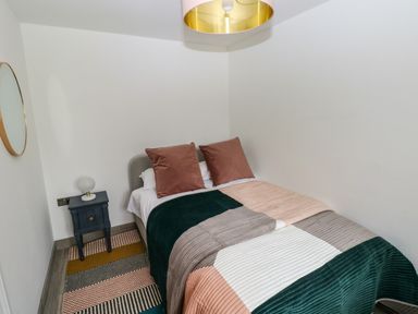 A bedroom with a double bed and striped quilt beside a bedside table with lamp at Folly Cottage in Llanteg near Saundersfoot