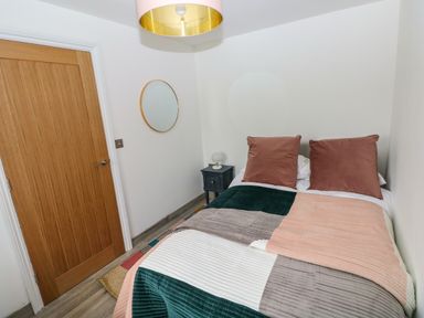 A bedroom with a bed bedspread pillows a wooden door a round wall mirror and a nightstand with a lamp at Folly Cottage Llanteg near Saundersfoot
