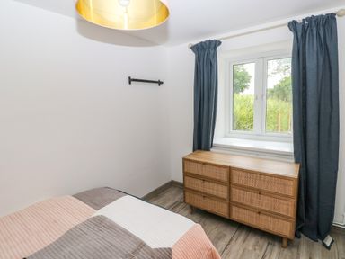 A bedroom with a bed covered by a quilt and a wooden drawer under a window with curtains at Folly Cottage in Llanteg near Saundersfoot