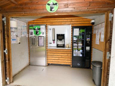 A wooden kiosk with a coffee machine vending machine and stainless steel door at Folly Cottage in Llanteg near Saundersfoot