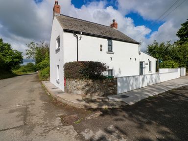 A white detached house on a corner with a stone wall and bushes beside a road at Folly Cottage Llanteg near Saundersfoot