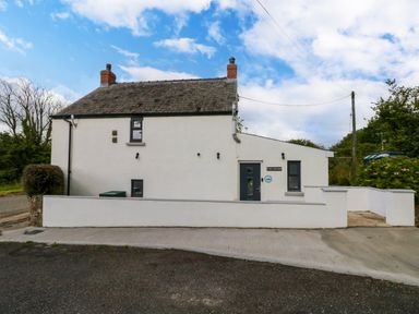 Exterior view of a white cottage with chimney stacks and a stone wall at Folly Cottage in Llanteg near Saundersfoot