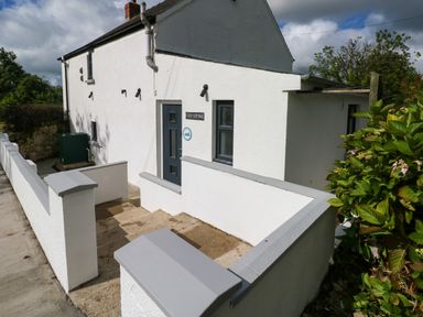 The exterior of a white cottage with a gray door and window at Folly Cottage in Llanteg near Saundersfoot