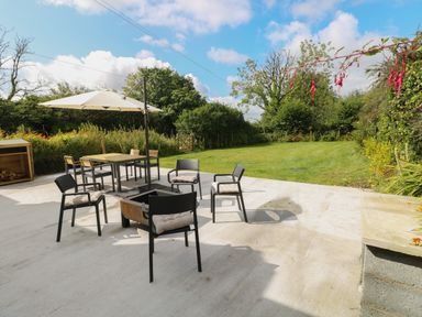 An outdoor patio with chairs around a fire pit and a table with an umbrella in a garden at Folly Cottage in Llanteg near Saundersfoot