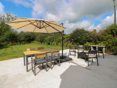 A patio with a table and chairs under a large umbrella and additional chairs around a fire pit at Folly Cottage in Llanteg near Saundersfoot