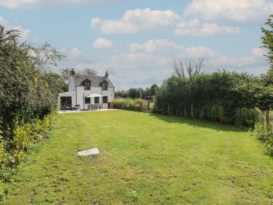 A white two-story house with a patio and outdoor furniture in a large grassy garden at Folly Cottage in Llanteg near Saundersfoot