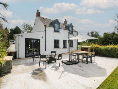 A white two-story house with black window frames a patio with chairs tables and a large umbrella at Folly Cottage in Llanteg near Saundersfoot