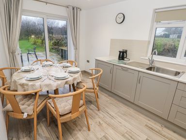 A kitchen with a round dining table set for six and a countertop with a kettle at Folly Cottage in Llanteg near Saundersfoot