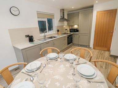 A kitchen with grey cabinets and a dining table with plates and glasses at Folly Cottage in Llanteg near Saundersfoot