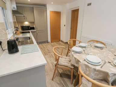 A kitchen and dining area with wooden chairs around a table set with plates and glasses at Folly Cottage Llanteg near Saundersfoot