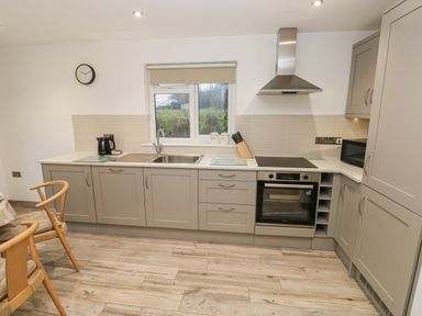 A kitchen with grey cabinets a stainless steel oven a sink a microwave and chairs at Folly Cottage in Llanteg near Saundersfoot
