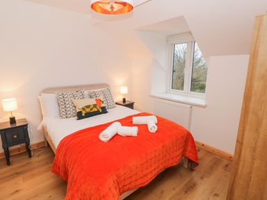 A bedroom with a bed covered by an orange blanket and pillows a window two bedside tables with lamps and a wooden wardrobe at Folly Cottage in Llanteg near Saundersfoot