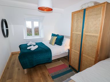 A bedroom with a bed with teal bedding a wooden wardrobe a colorful rug and a window at Folly Cottage in Llanteg near Saundersfoot