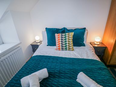 A bedroom with a bed with teal pillows and quilt and bedside tables with lamps at Folly Cottage in Llanteg near Saundersfoot