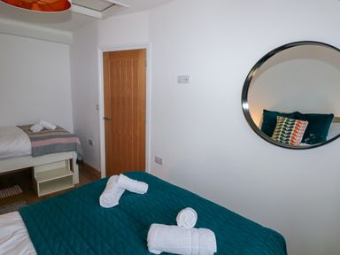 A bedroom with two beds towels on the beds a round mirror on the wall and a wooden door at Folly Cottage in Llanteg near Saundersfoot
