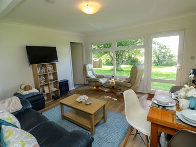 A living room with black sofa two cream armchairs wooden coffee table and dining table with chairs at 61 Norton Park in Dartmouth