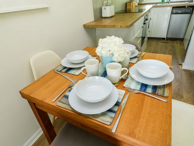 A wooden dining table set for four with white dishes and mugs and a vase with white flowers in a kitchen at 61 Norton Park Dartmouth