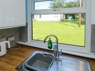 A kitchen sink with a faucet soap and dishwashing liquid by a window showing a grassy yard at 61 Norton Park in Dartmouth