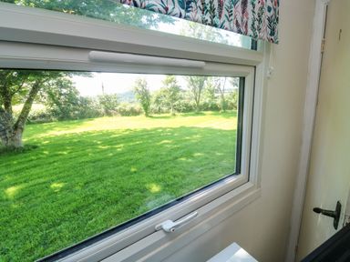 A window looking out onto a green lawn with trees and a patterned window blind at 61 Norton Park in Dartmouth