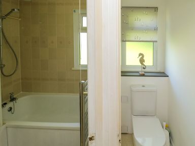 A bathroom with a bathtub and shower on the left and a toilet with a window above it on the right at 61 Norton Park in Dartmouth