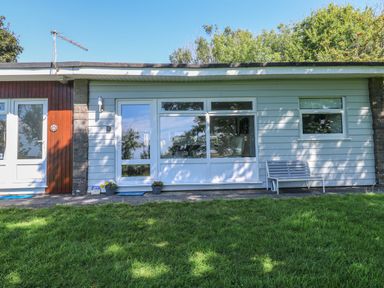 Exterior view of a single-story house with white siding a glass door large window two flower pots a bench and green grass at 61 Norton Park in Dartmouth