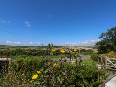 A rural landscape with fields hills a curving road and wildflowers by a wooden gate at 61 Norton Park in Dartmouth