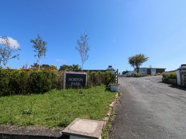 The entrance to Norton Park with a sign and a paved road leading to buildings in Dartmouth