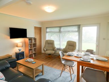 A living room with leather chairs a wooden dining table set with dishes and a wall mounted television at 61 Norton Park in Dartmouth