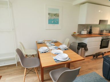 A dining table set with plates bowls and glasses in a kitchen with white cabinets and a small dog on the floor at 61 Norton Park in Dartmouth