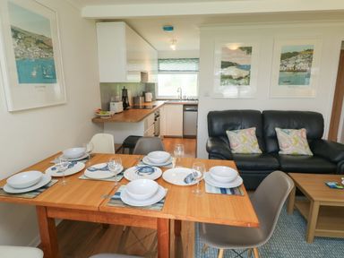 A dining table set with plates and glasses next to a kitchen with wooden counters and a living area with a black leather sofa at 61 Norton Park in Dartmouth