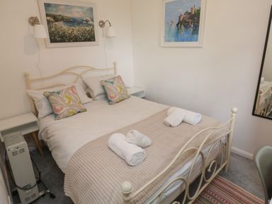 A bedroom with a bed with pillows and rolled towels bedside tables a heater paintings on the wall and a mirror at 61 Norton Park in Dartmouth
