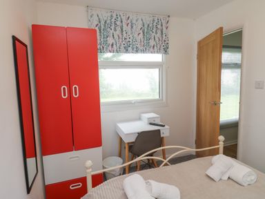 A bedroom with a red and white wardrobe desk with a chair window with floral blind and a bed with towels at 61 Norton Park in Dartmouth