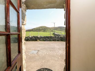 An open door showing a view of a stone wall green fields and hills at Ereiniog 2 in Tremadog
