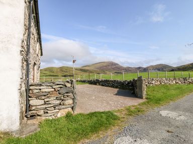 A stone wall and driveway next to a white building with mountains and green fields in the background at Ereiniog 2 in Tremadog