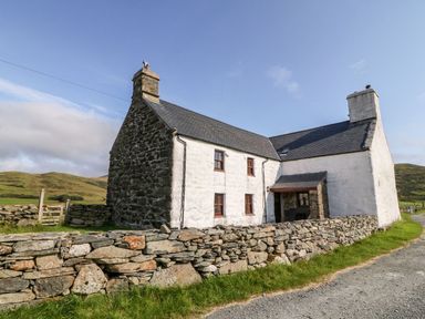 A stone and whitewashed house with chimneys and a low stone wall beside a dirt road at Ereiniog 2 in Tremadog