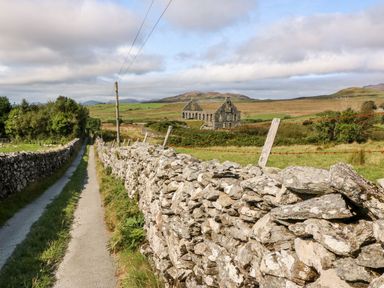 A narrow paved path with stone walls on both sides leading to a ruined stone building in a rural area at Ereiniog 2 in Tremadog