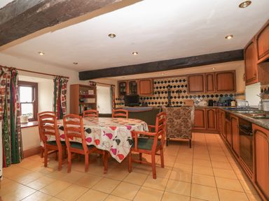 A kitchen with wooden cabinets a tiled floor a dining table with chairs and a stove at Ereiniog 2 in Tremadog