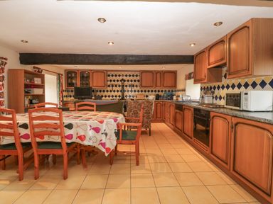 A kitchen and dining area with wooden cabinets a dining table with chairs and tiled floor at Ereiniog 2 in Tremadog