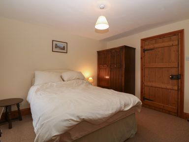 A bedroom with a double bed white bedding wooden wardrobe wooden door and a small bedside table at Ereiniog 2 in Tremadog
