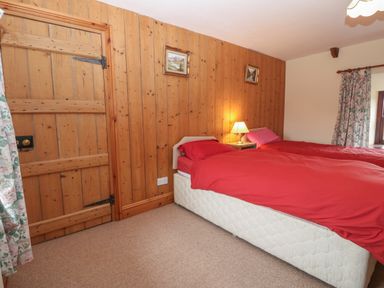 A bedroom with two single beds with red bedding a wooden door wooden panelled wall and floral curtains at Ereiniog 2 in Tremadog
