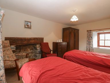 A bedroom with two red beds red and floral armchairs a wooden wardrobe and chest of drawers with floral curtains at Ereiniog 2 in Tremadog