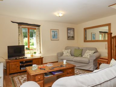 A living room with a wooden coffee table and TV stand two sofas a window and a large wall mirror at Peace Cottage Queens Nympton near South Molton