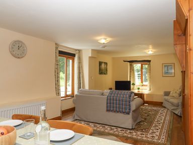 A living room with two beige sofas a TV and a rug near windows and a dining table at Peace Cottage Queens Nympton near South Molton