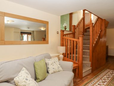 A sitting area with a sofa and cushions next to a carpeted staircase with wooden railing and a wall mirror at Peace Cottage Queens Nympton near South Molton