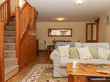 A living room with a beige sofa and wooden coffee table next to carpeted stairs at Peace Cottage in Queens Nympton near South Molton